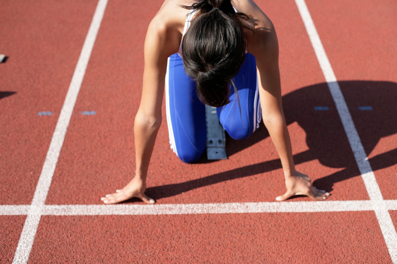 services-03 A female athlete crouches at the starting line, ready to sprint on a sunny day.