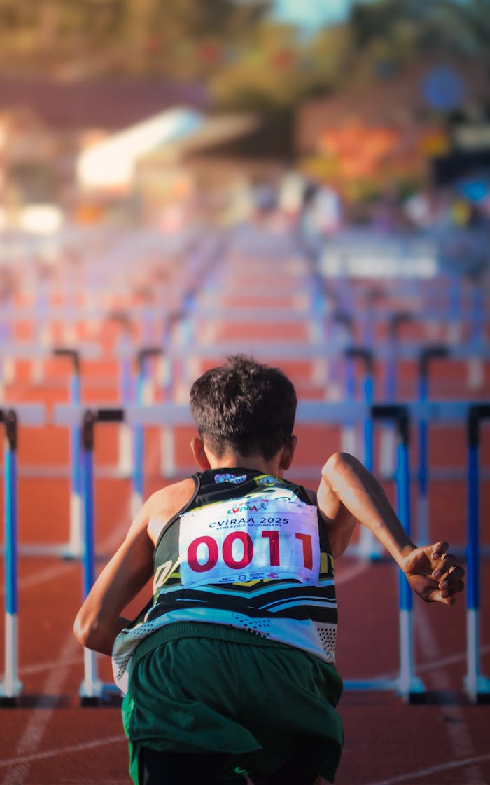 services-02 A young runner with numbered bib preparing for a hurdle race on a sunny track.
