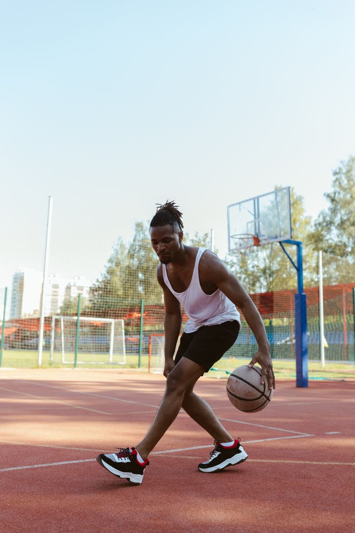 our-story Young man dribbling basketball on outdoor court during daytime.